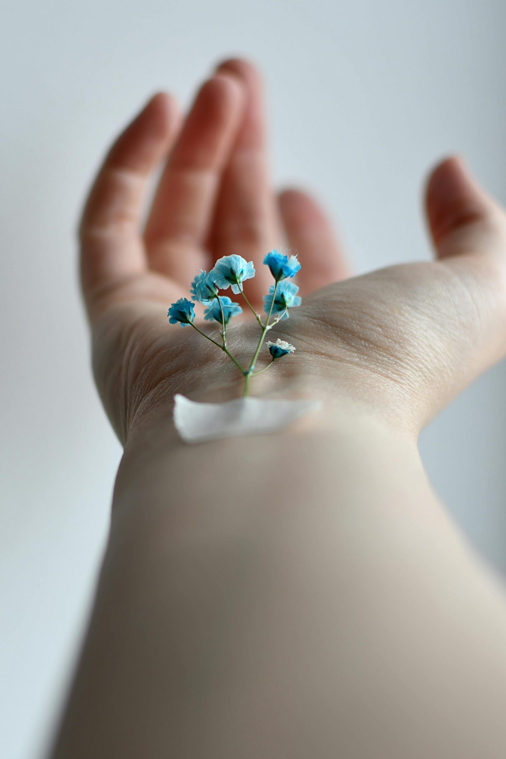 Close-up of a hand with small blue flowers attached by tape, emphasizing delicacy and nature.